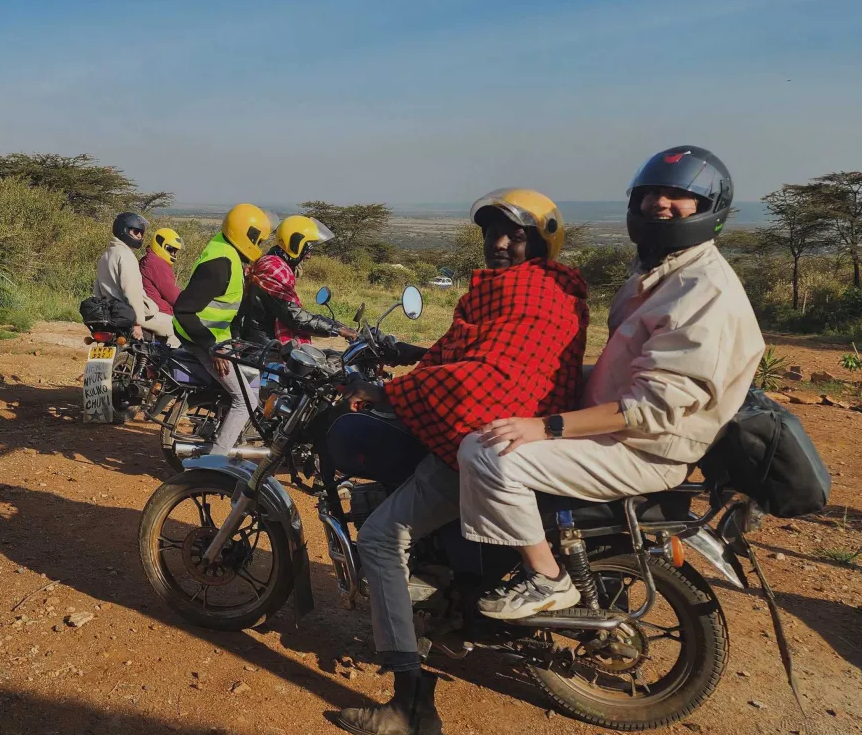 Ospiti sul sellino posteriore di moto lungo una pista di terra rossa nelle terre masai.